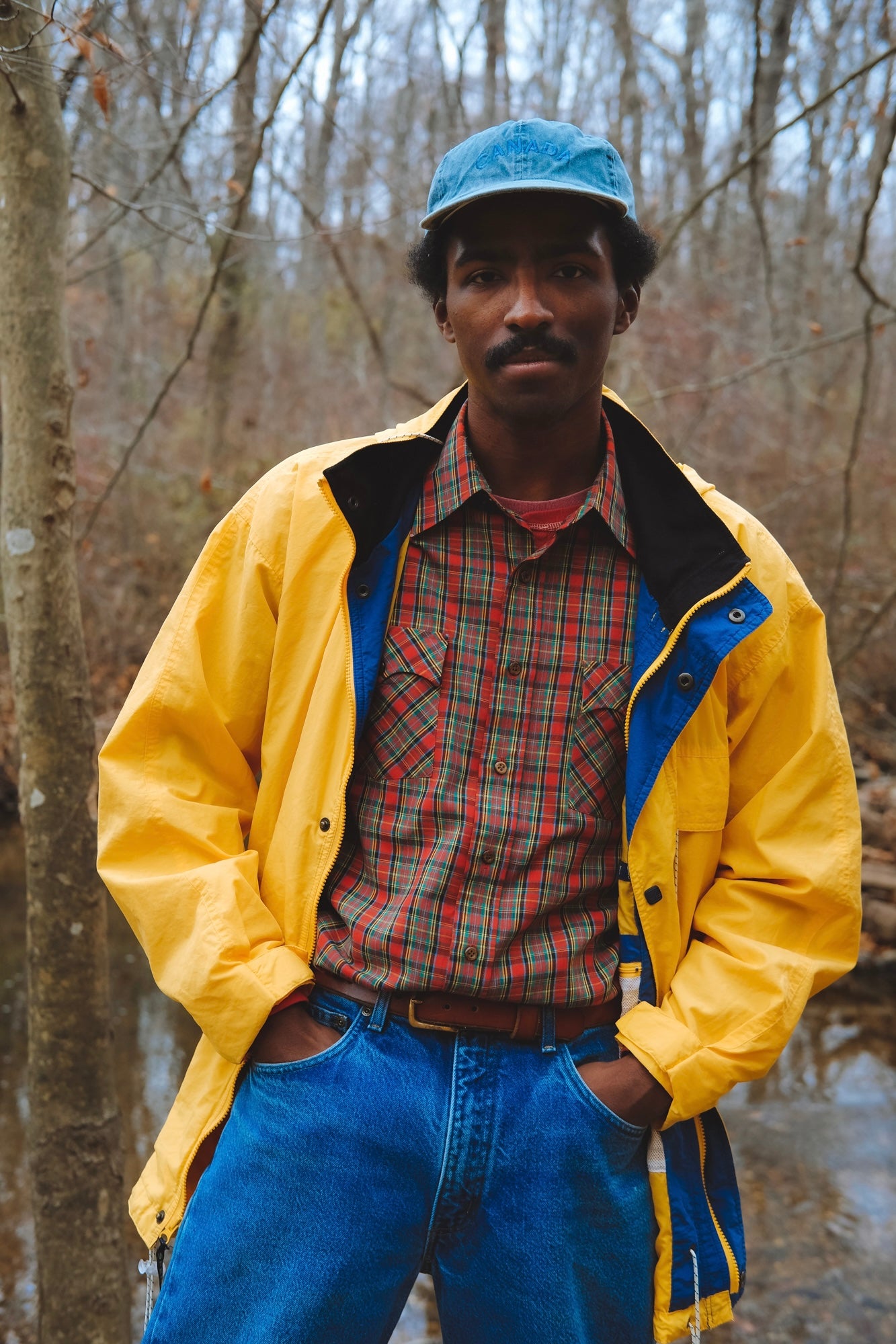 Male model wears red plaid western-style shirt under a long yellow windbreaker.