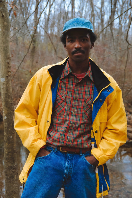 Male model wears red plaid western-style shirt under a long yellow windbreaker.