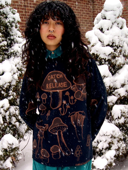 Female model wears one-of-a-kind long-sleeve painted tee with a design of various mushrooms and the text "Catch & Release"