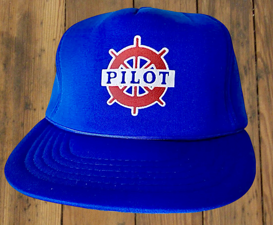 Blue cap with extra-high crown, firm foam polyester fabric, and steering wheel graphic with "pilot" written out. 