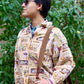 Model wears tan-colored button-up long sleeve shirt with all-over print including farmer's market, culinary & fishing images