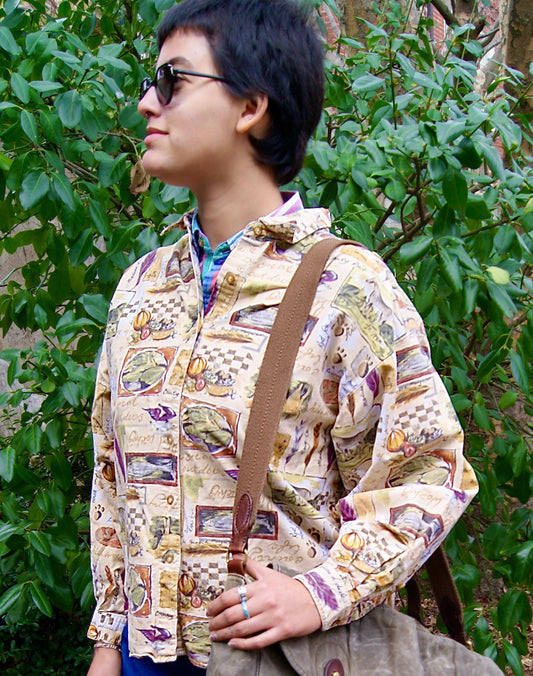 Model wears tan-colored button-up long sleeve shirt with all-over print including farmer's market, culinary & fishing images