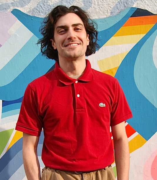 Model wears dark red polo shirt with classic alligator emblem on chest.