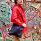 Male model holds navy blue waxed canvas tote bag while standing in an alley of mosiac tile artwork.